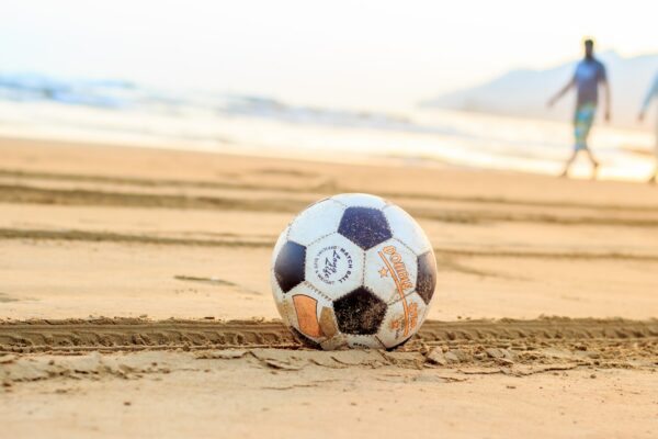 soccer ball on brown sand with two man in the background